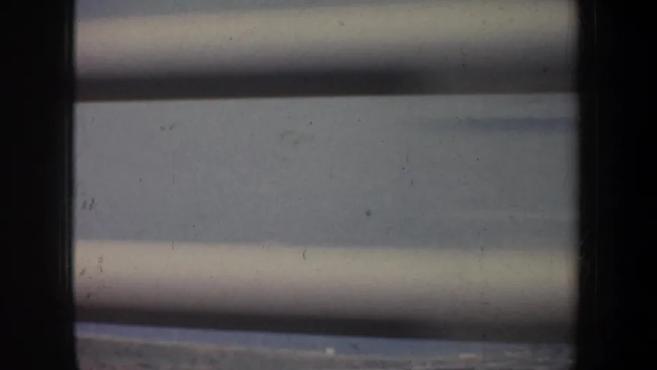 A 1957 8mm coastal view shows blue water through horizontal slats, with only a small edge of shoreline visible.