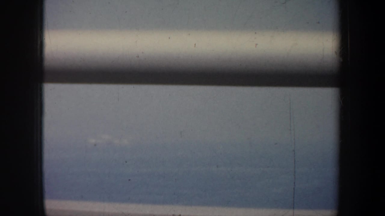 Window frame and rails cross a soft view of water and distant land.