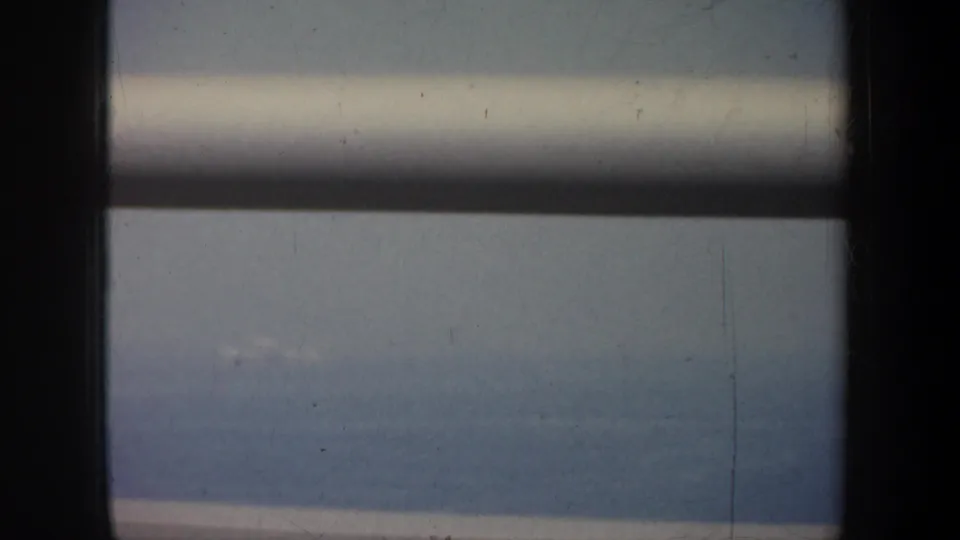 Muted 8mm frame from a moving vehicle, with window rails over a San Francisco-area water and shoreline view.