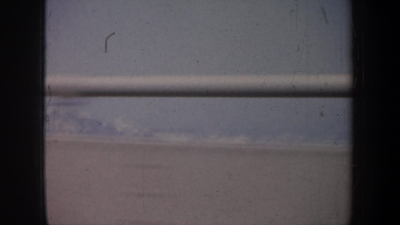 Dark window frame and bridge railing seen from a moving car with hazy sky beyond.