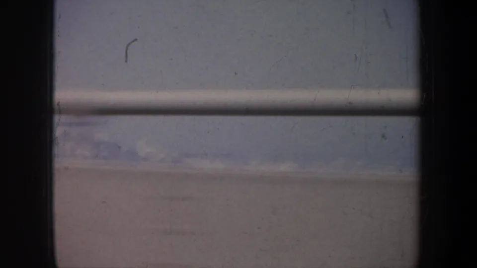 1957 San Francisco home-movie frame showing a bridge railing through a dark car-window edge, with hazy sky and distant landscape beyond.