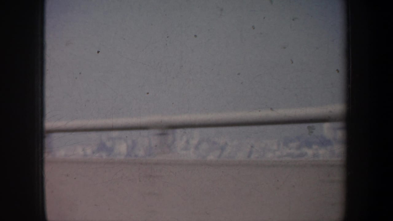 Soft 1957 San Francisco skyline view through vehicle framing, with water and distant buildings partly obscured by blur and film wear.