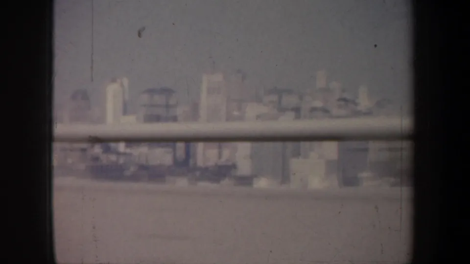 Distant San Francisco buildings and waterfront forms appear through a vehicle window or railing, with muted color and visible film scratches.