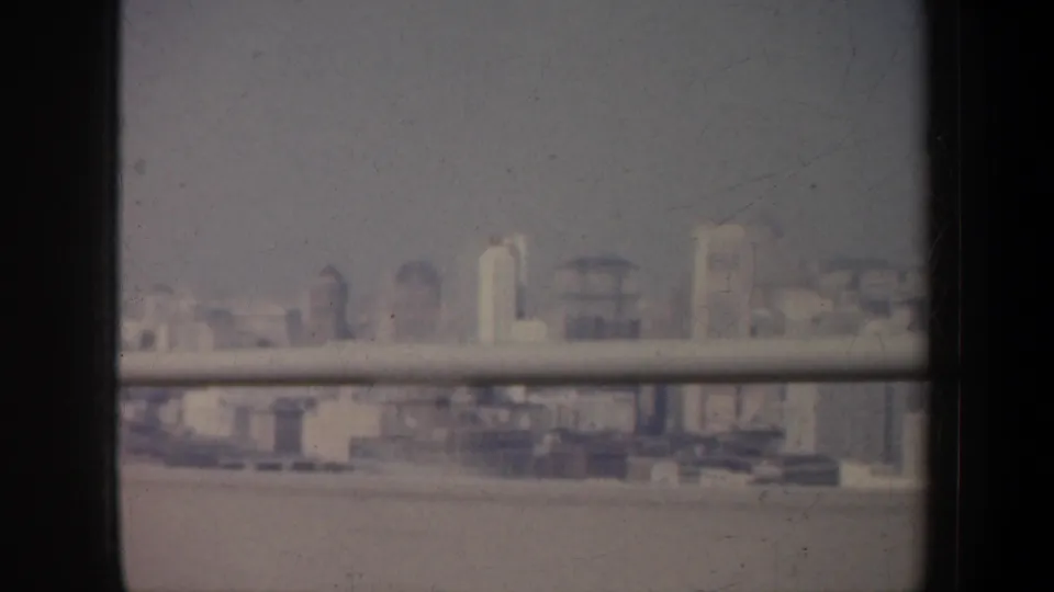 A low-contrast 8mm view of San Francisco buildings across water, framed by dark vehicle edges and a horizontal rail or window bar.