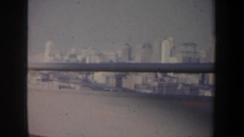 The 1957 San Francisco cityscape remains distant and hazy, with water below and dark window or railing elements crossing the frame.