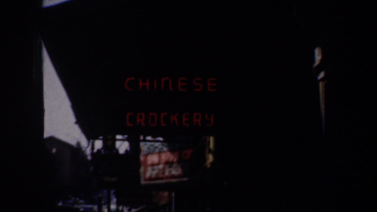 Dark street view with red Chinese crockery sign above shadowed storefronts.