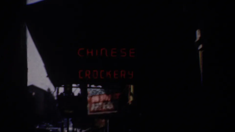1957 San Francisco home-movie frame showing a red Chinese crockery sign over a dim nighttime street.