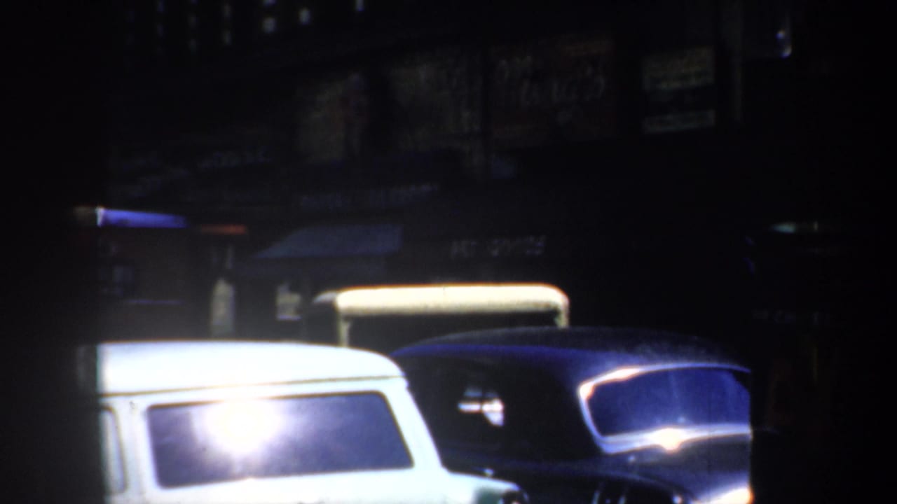 White station wagon and dark cars parked along a dim commercial street.