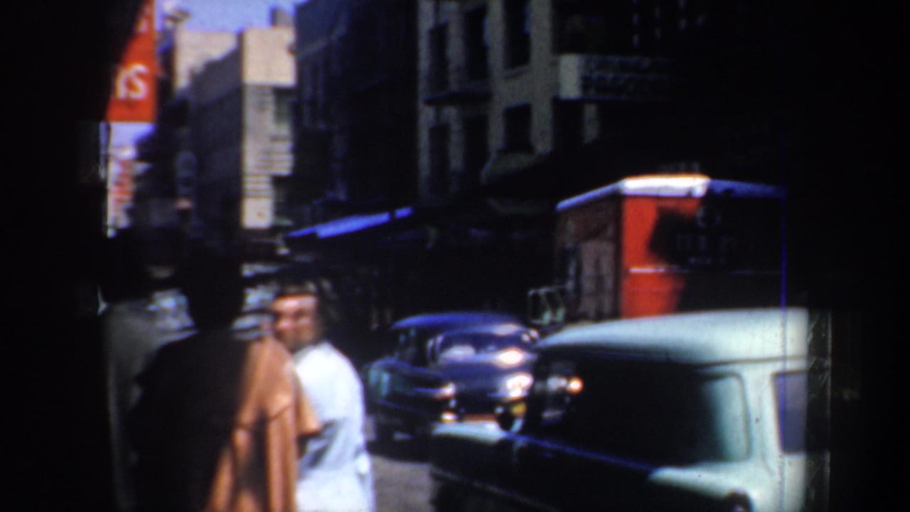 Pedestrians and classic cars on a shaded Chinatown street with storefront awnings.