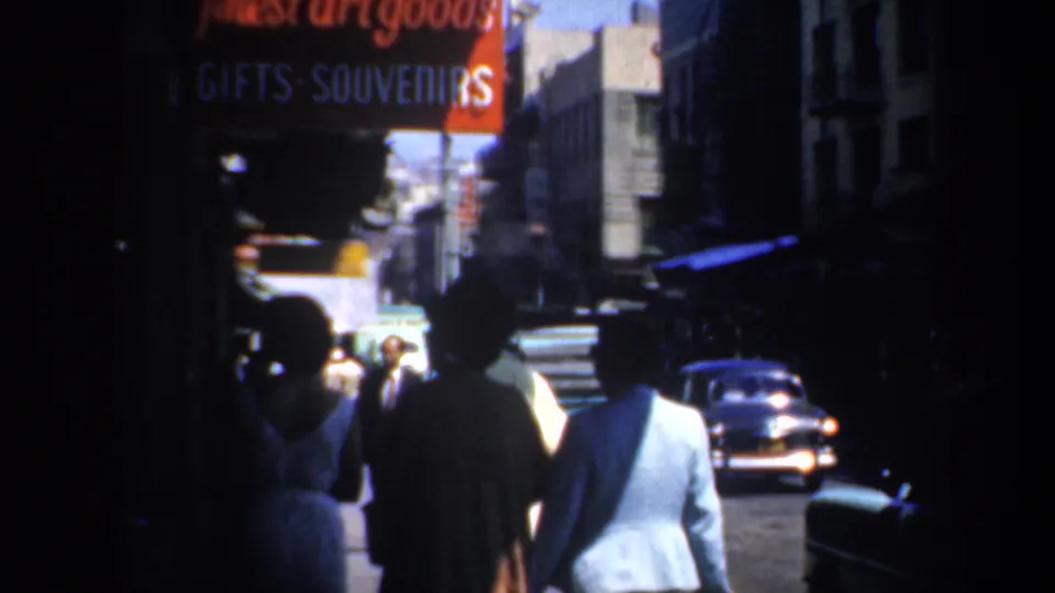 San Francisco Chinatown sidewalk in 1957 with pedestrians walking under a red sign advertising art goods, gifts, and souvenirs.