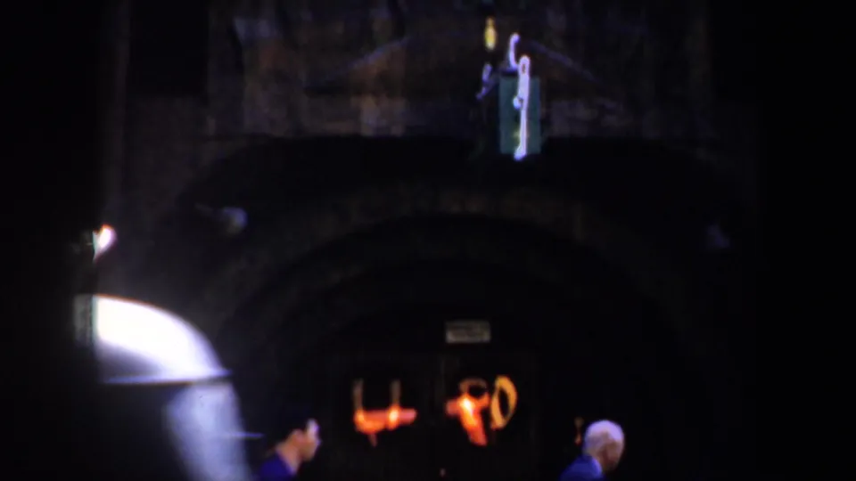 Two men in dark clothing pass a dim arched entrance in 1957 San Francisco, with warm interior lights visible beyond the doorway.