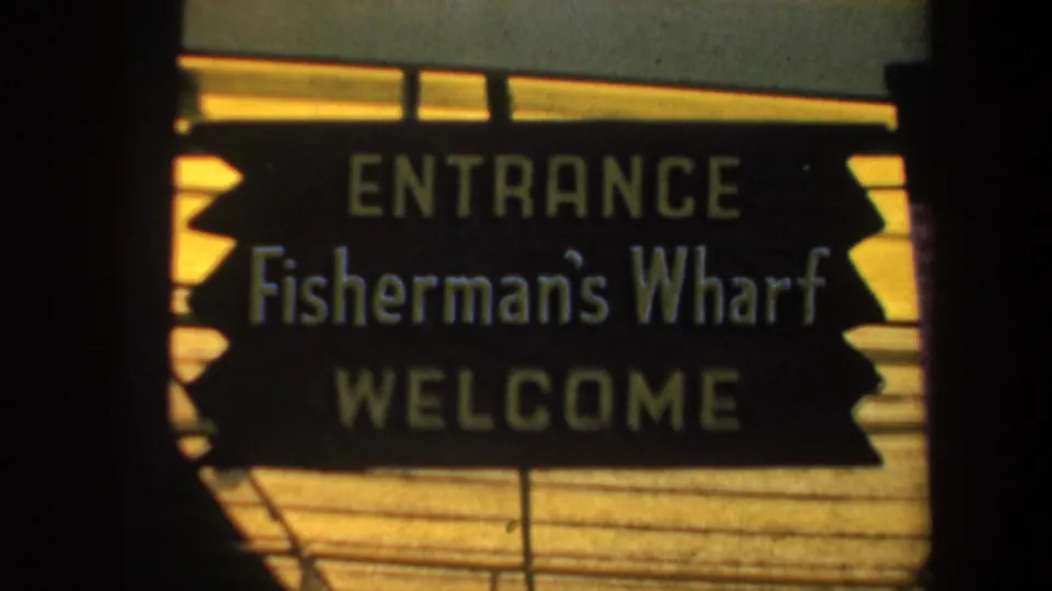 Close 1957 San Francisco view of the Fisherman's Wharf entrance sign with readable welcome text and soft 8mm focus.