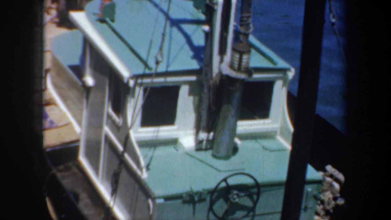 Small white cabin boat with teal roof docked beside blue water and wooden planks.