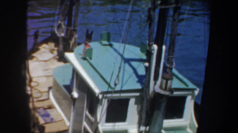 1957 San Francisco frame with the boat's teal cabin roof, dock planks, rigging, and water partly obscured by dark frame edges.