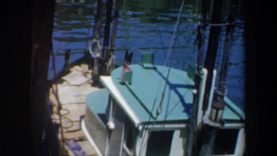 1957 San Francisco home-movie frame showing the teal-roofed cabin boat, dock, rigging, and water from a slightly shifted handheld angle.