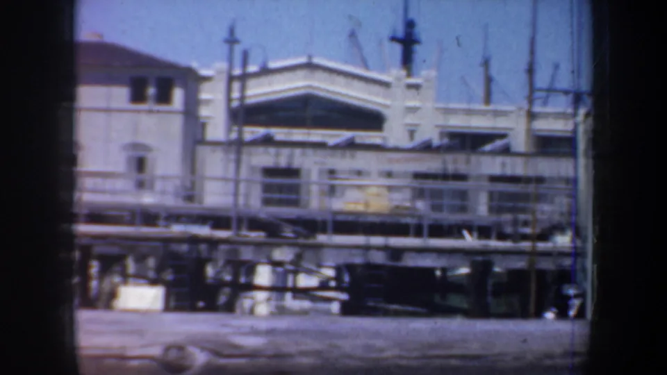 1957 San Francisco frame showing a white waterfront building, railings, pilings, and pier structures in soft home-movie focus.
