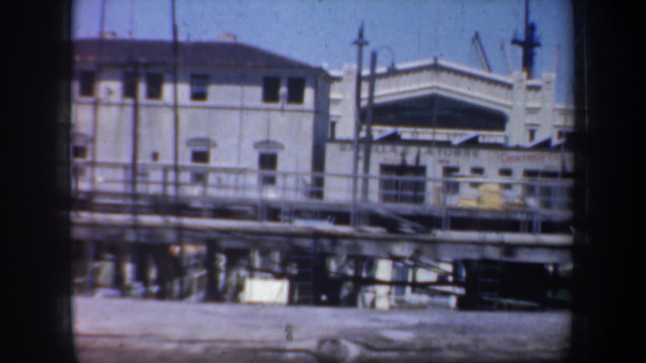 Light grey waterfront building behind pier railings under a blue sky.