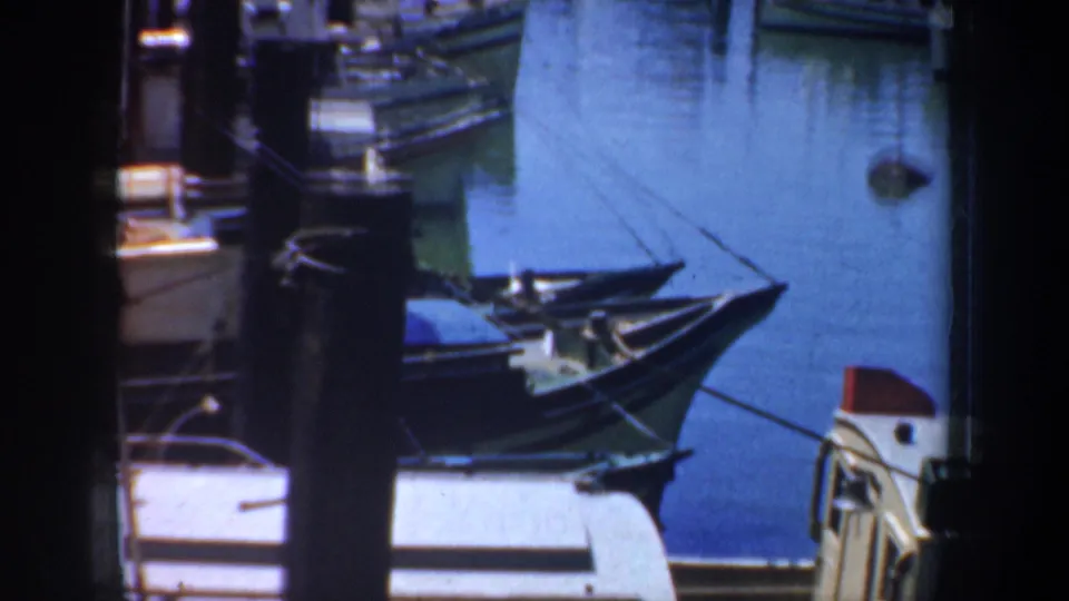 1957 San Francisco harbor frame with boat bows, dock posts, ropes, and a light-colored vessel edge in the foreground.