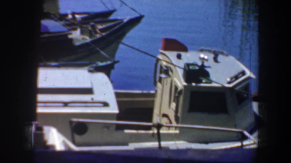 1957 San Francisco waterfront view of a light blue and white houseboat near moored boats and dock structures.
