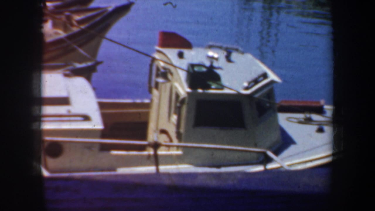 1957 San Francisco harbor frame showing a small cabin boat at the dock, blue water, and visible 8mm film edge shadows.