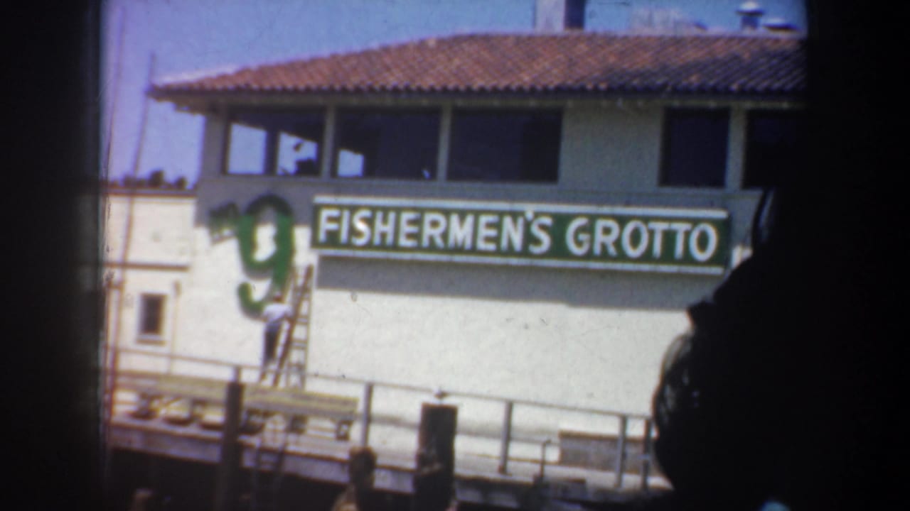 Fishermen's Grotto sign on a waterfront building with a man on a ladder.