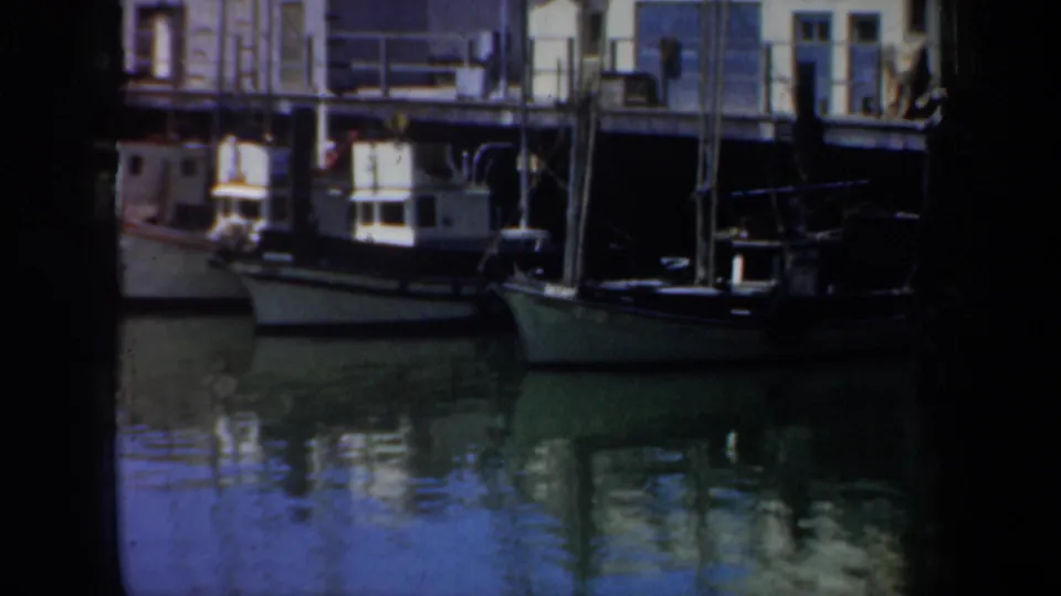 1957 San Francisco dock scene with small fishing boats, pier pilings, railings, and reflections on calm water.