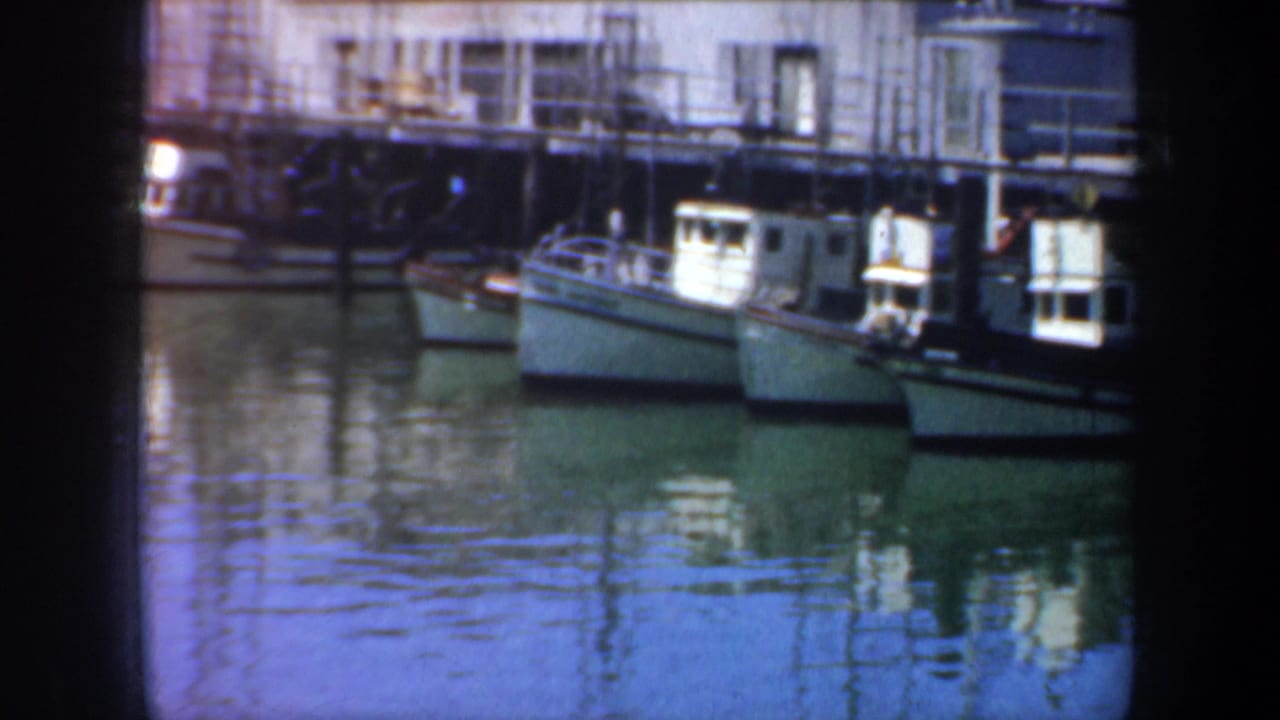 1957 San Francisco waterfront view with docked boats, pier structures, and soft reflections in bay water.