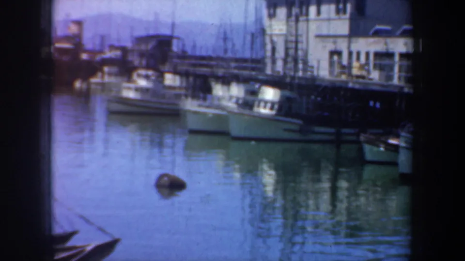 San Francisco waterfront scene showing moored boats near pier buildings, with calm water and visible home-movie film edges.