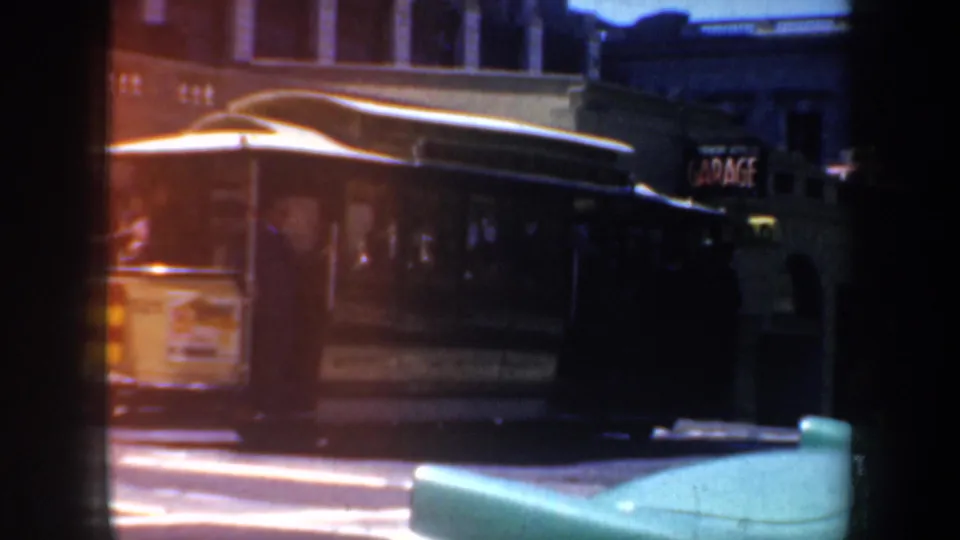 1957 San Francisco street view with a cable car passing near arched buildings and a period automobile in the foreground.