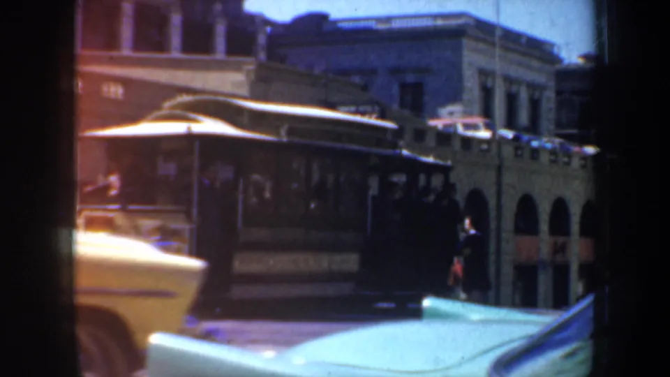 San Francisco cable car street scene with a yellow car in the foreground, arched architecture, and soft 8mm color fading.