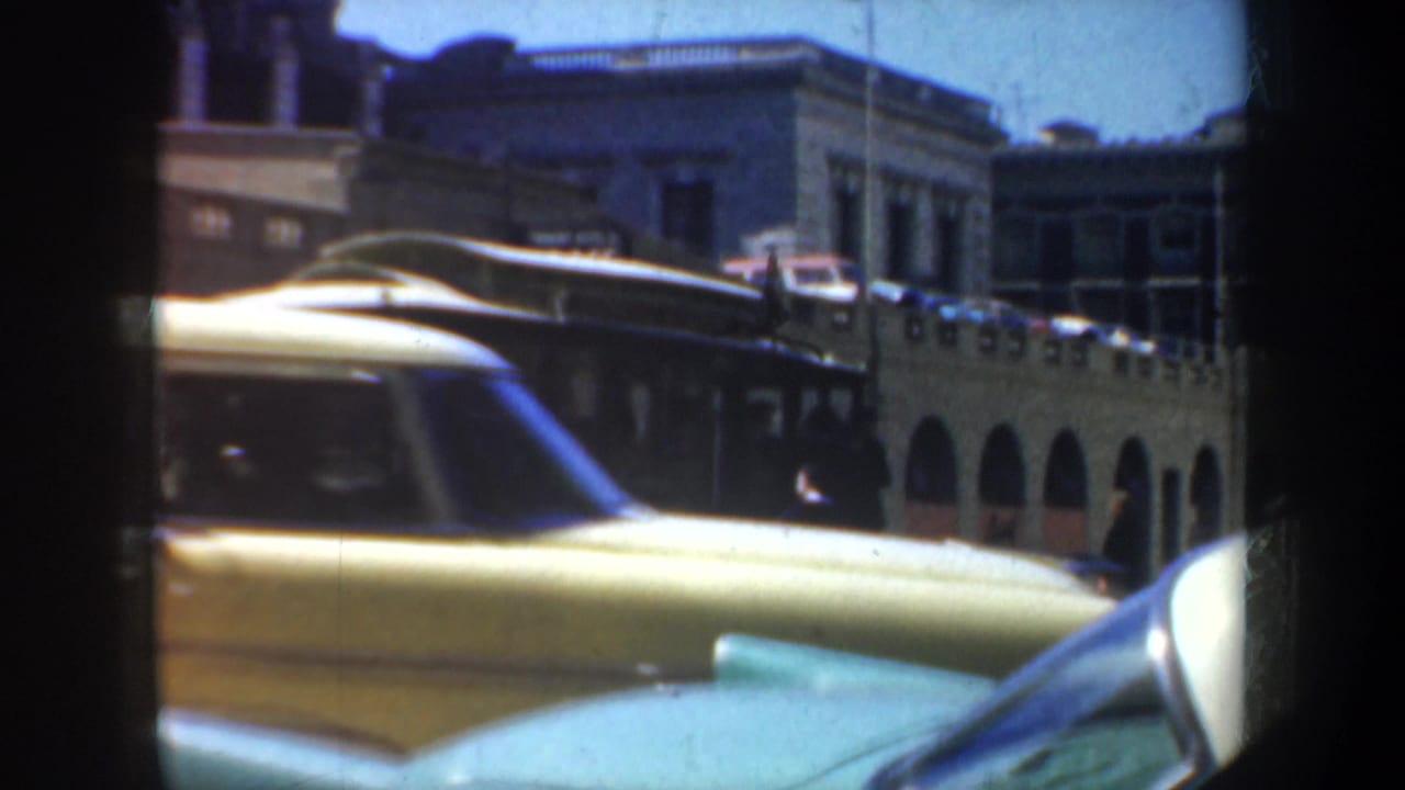 1957 San Francisco street view with mid-century cars in the foreground, a trolley behind them, and arched urban architecture in bright daylight.