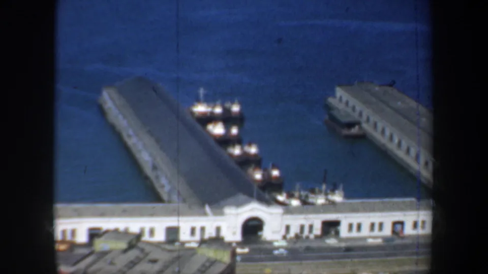 Elevated 1957 San Francisco waterfront view with long piers, docked boats, harbor water, and a road along the shoreline.