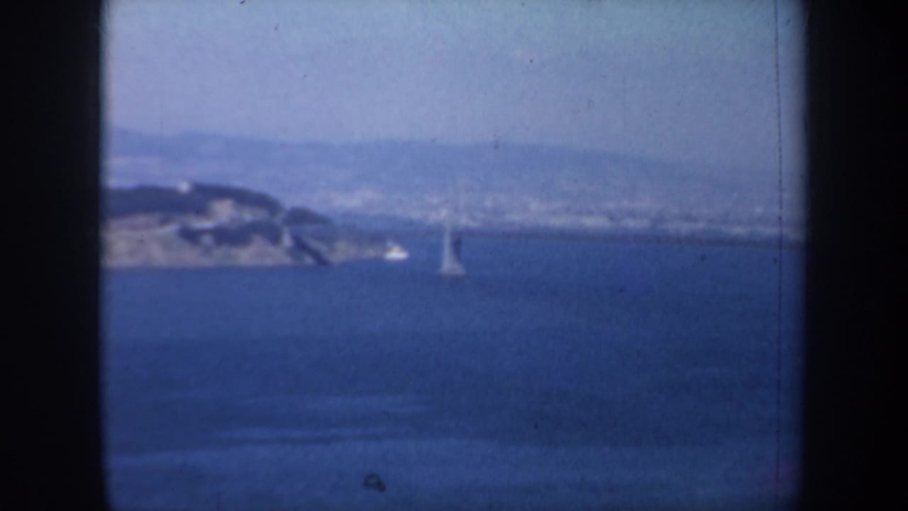 Hazy bay view with distant bridge tower, sailboat, shoreline, and dark 8mm frame edges.