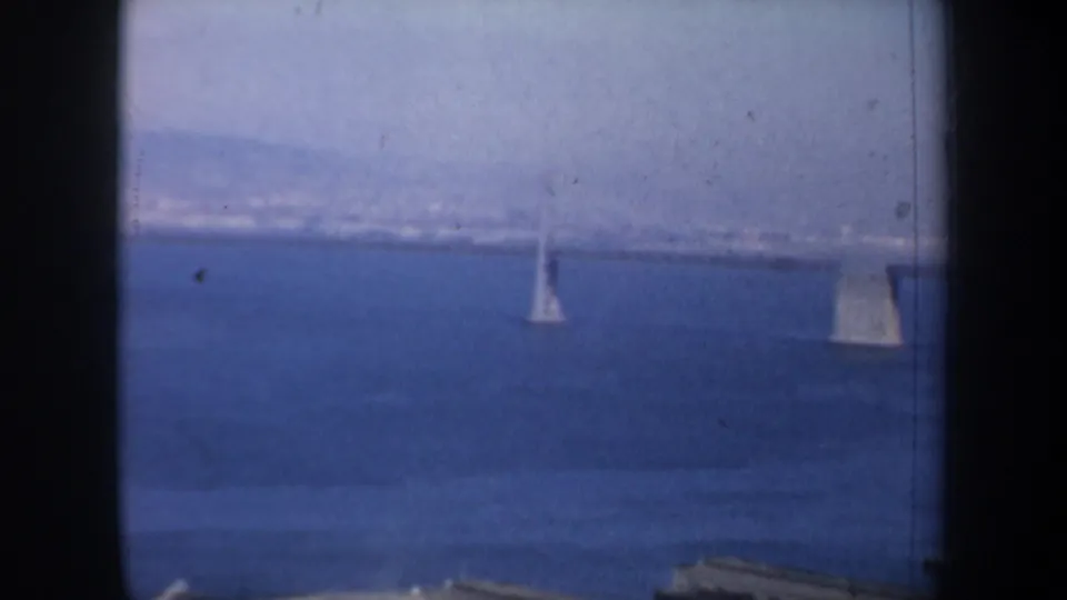 1957 San Francisco Bay footage shows a bridge tower and shoreline across blue water, softened by haze and 8mm texture.