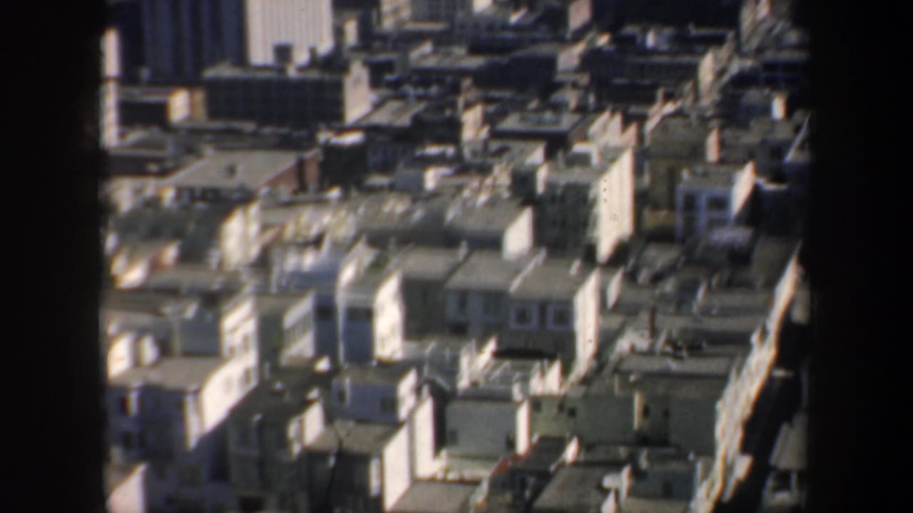 1957 San Francisco downtown rooflines and towers viewed from above, partly obscured by dark window or film-gate edges.
