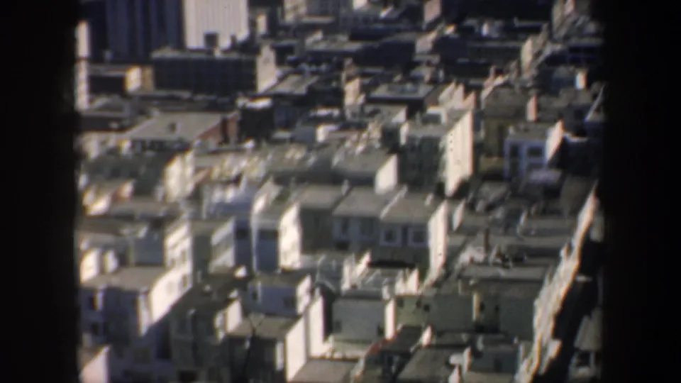 1957 San Francisco downtown rooflines and towers viewed from above, partly obscured by dark window or film-gate edges.