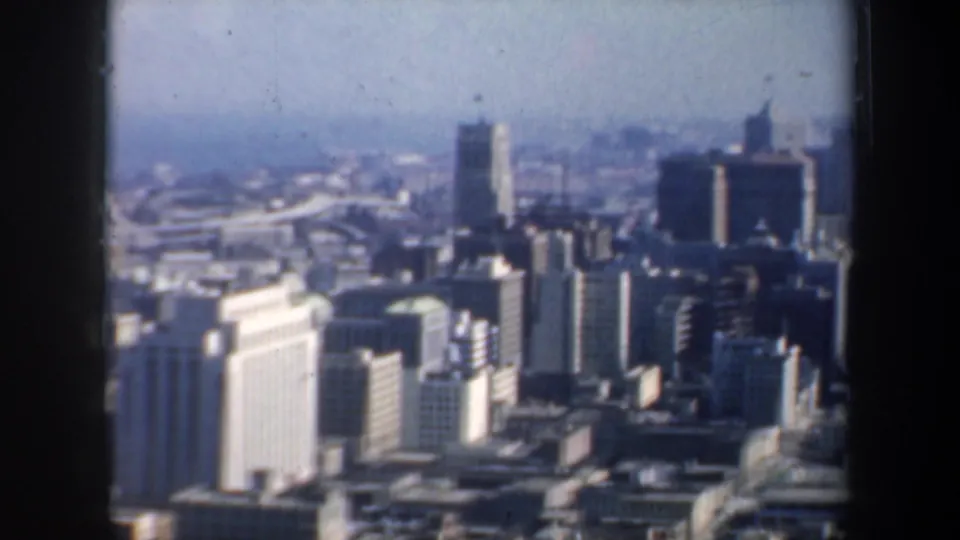 1957 San Francisco skyline view with high-rises, a bright foreground building, distant haze, and possible waterfront beyond the downtown blocks.
