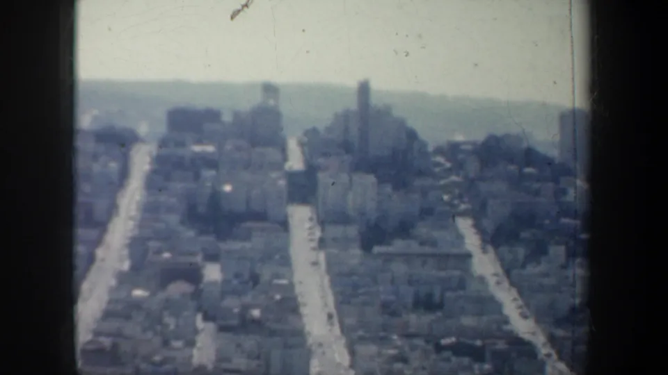 1957 San Francisco aerial view showing rooftops, receding streets, distant haze, and visible 8mm film-frame borders.