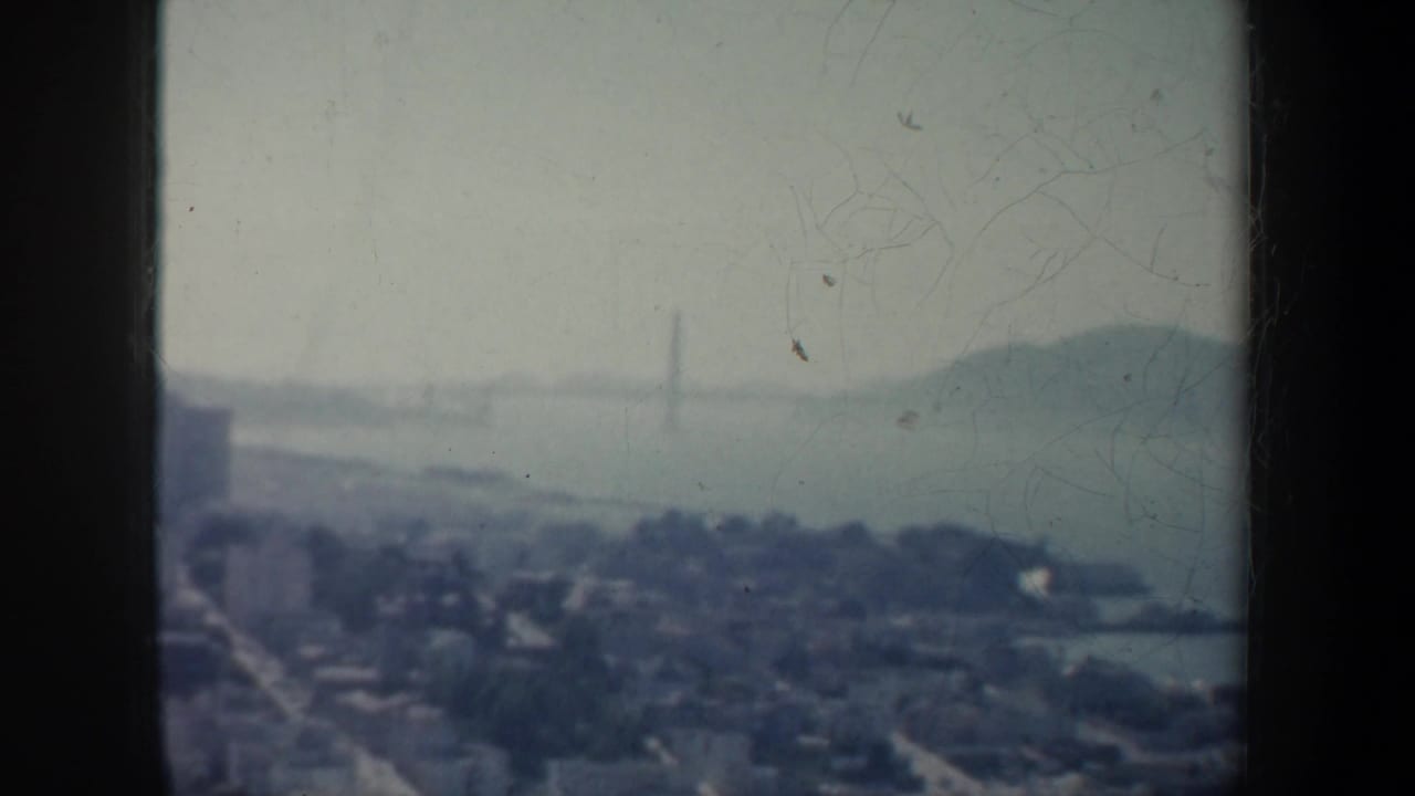 Hazy bay view with distant Golden Gate Bridge, shoreline, hills, and water.