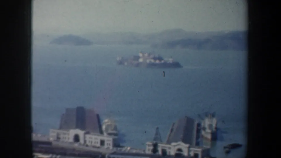 1957 San Francisco Bay view with Alcatraz Island offshore and waterfront structures in the foreground.