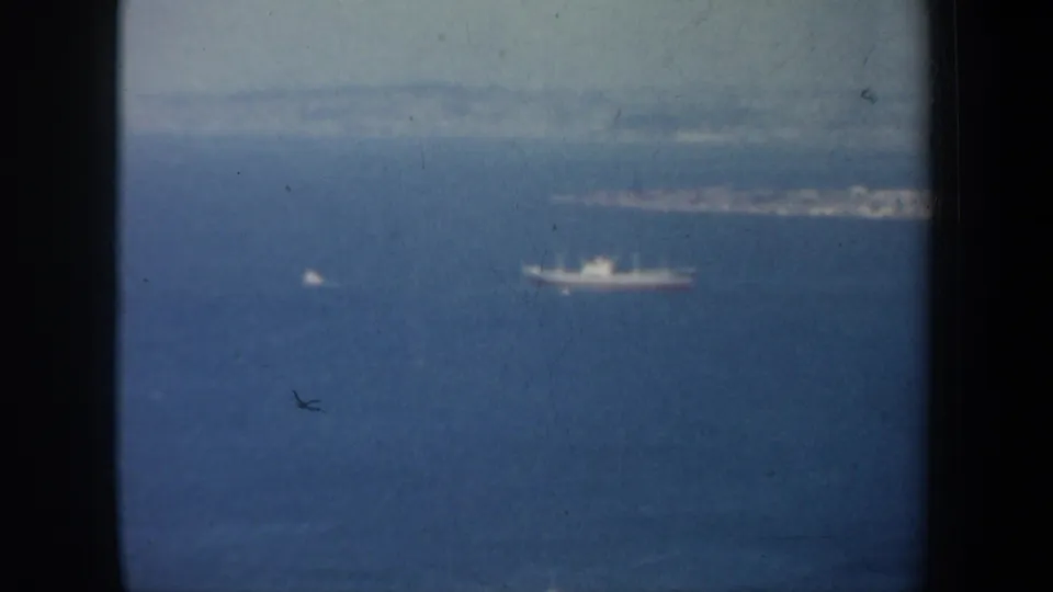 1957 San Francisco Bay shot showing a large vessel and smaller craft on hazy blue water, framed by dark vertical edges.