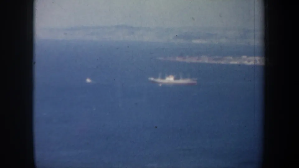1957 8mm San Francisco Bay view with a ship near the center, a small boat to the left, and soft shoreline beyond.