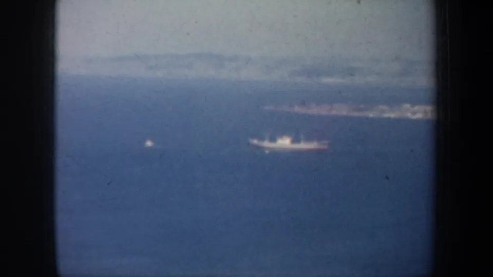 1957 San Francisco Bay frame with a distant vessel on blue water and a hazy shoreline or island mass behind it.