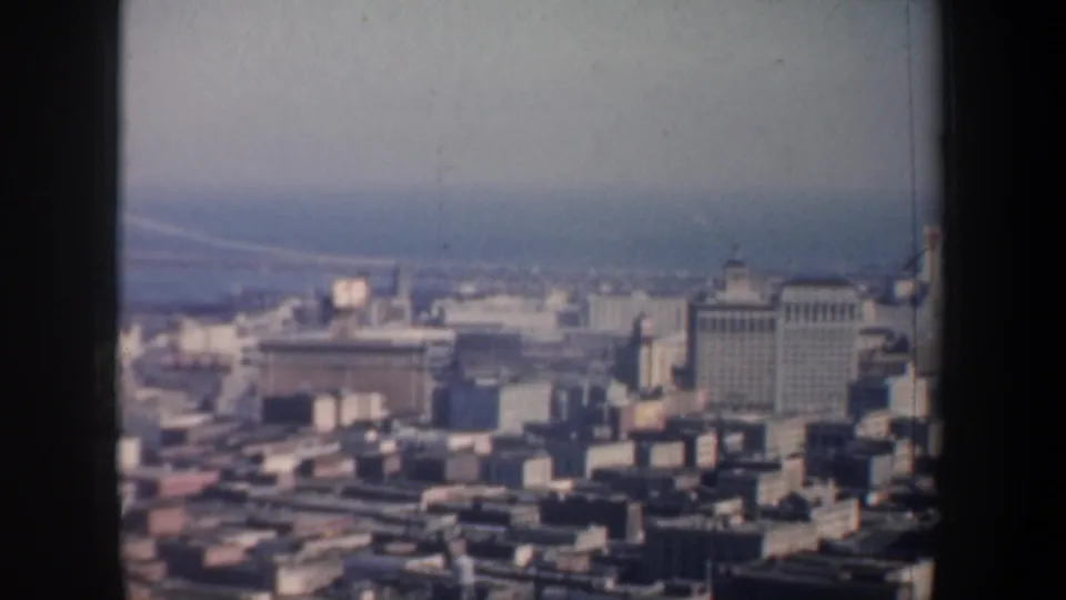 1957 8mm view from above San Francisco showing downtown buildings, bay water, and part of the Bay Bridge through soft focus.