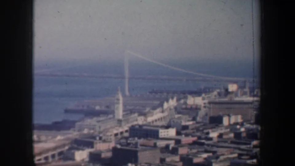 San Francisco's waterfront and Bay Bridge tower appear in a soft 1957 8mm frame with bay water behind the city.