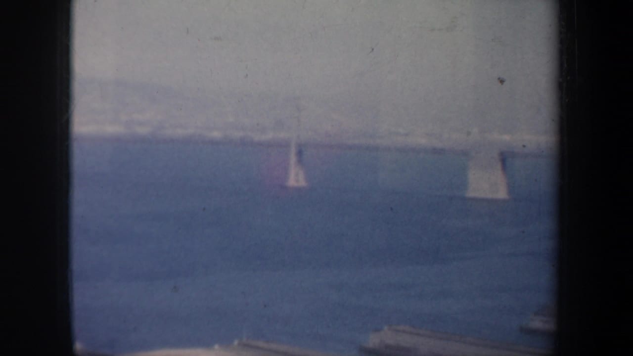 1957 San Francisco home-movie frame showing blue bay water, faint shoreline, distant sailboats, and heavy 8mm frame edges.