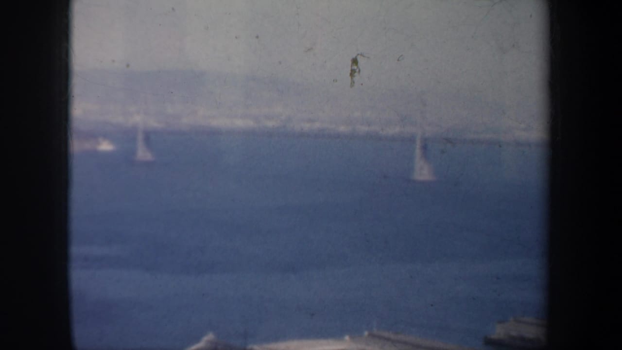 Blue water, faint bridge structure, and small sailboats in haze.