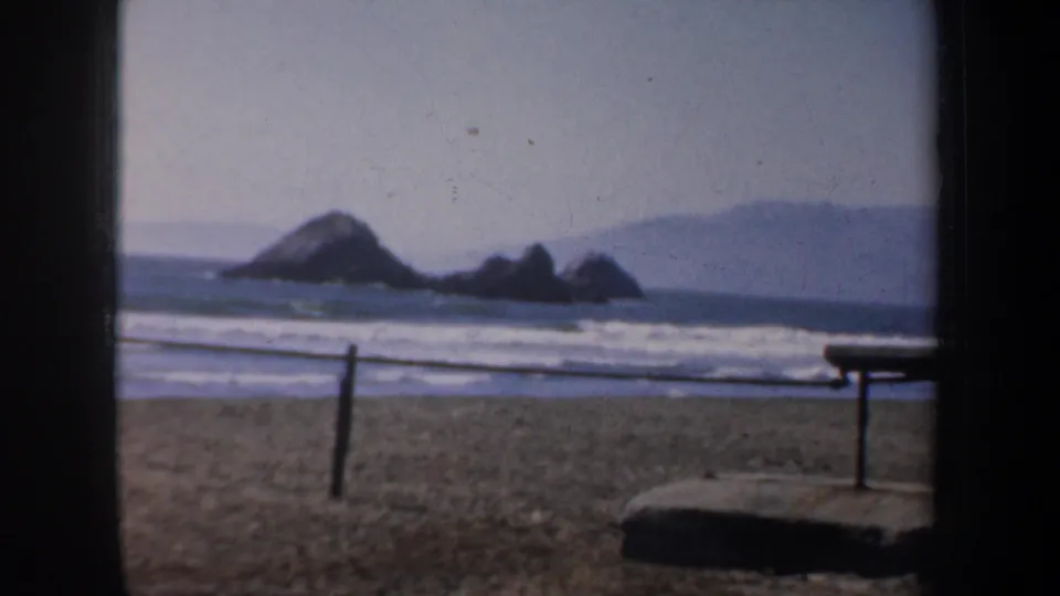 1957 San Francisco coastal home-movie view showing sandy beach, ocean surf, and rocky outcrops offshore.
