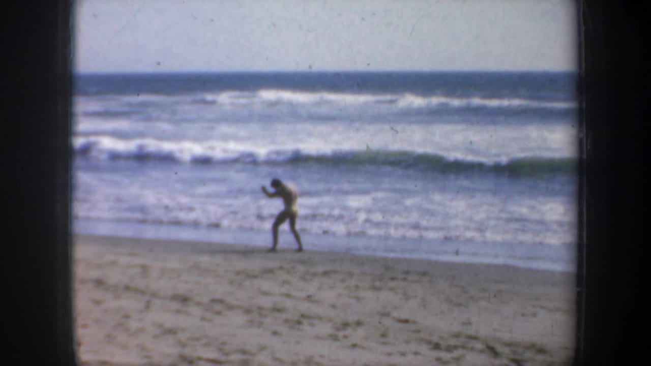 Man on a sandy beach practices boxing motions near rolling ocean waves.