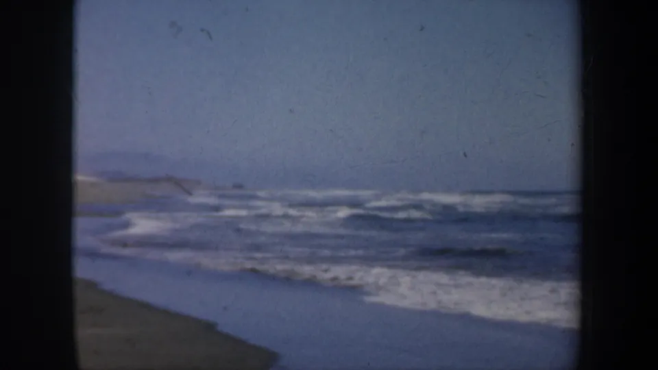 Soft 8mm beach view in San Francisco, showing waves, wet shoreline, open sand, and dark home-movie frame borders.